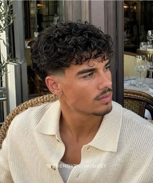 Curly fringe taper fade with defined Type 3A curls on a stylish man at a European café terrace.