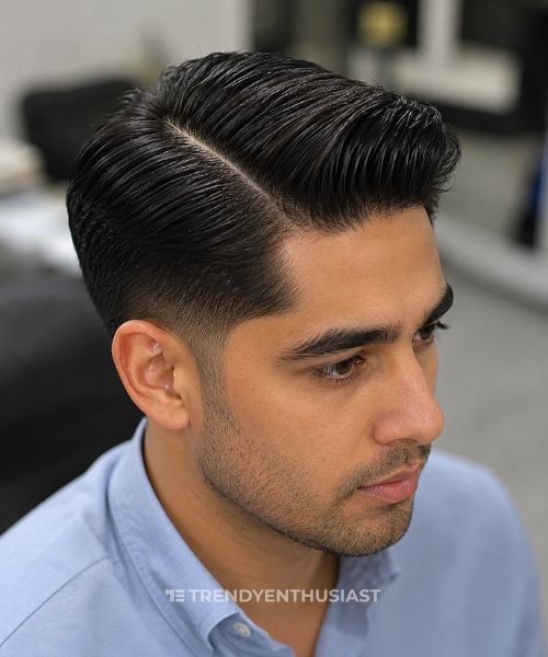 Man with a classic comb over, mid taper fade, and hard part, photographed in a blurred barbershop on an iPhone-style portrait.