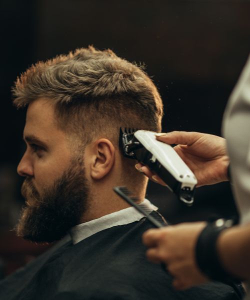 A barber uses clippers to give a man a fade haircut.