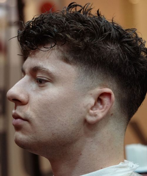 Profile of a person with curly dark hair styled with a taper fade on the sides.