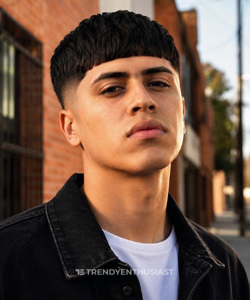 Low Fade Edgar haircut on a young man with a blunt fringe and clean low fade in an urban street portrait.