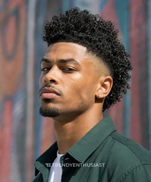 Afro-Caribbean man with a low fade mohawk featuring defined curly texture in a close-up portrait.