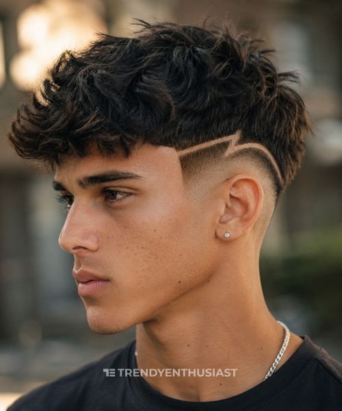 Teenage man with a low fade haircut featuring sharp geometric design lines and a textured messy top in a side-profile portrait.